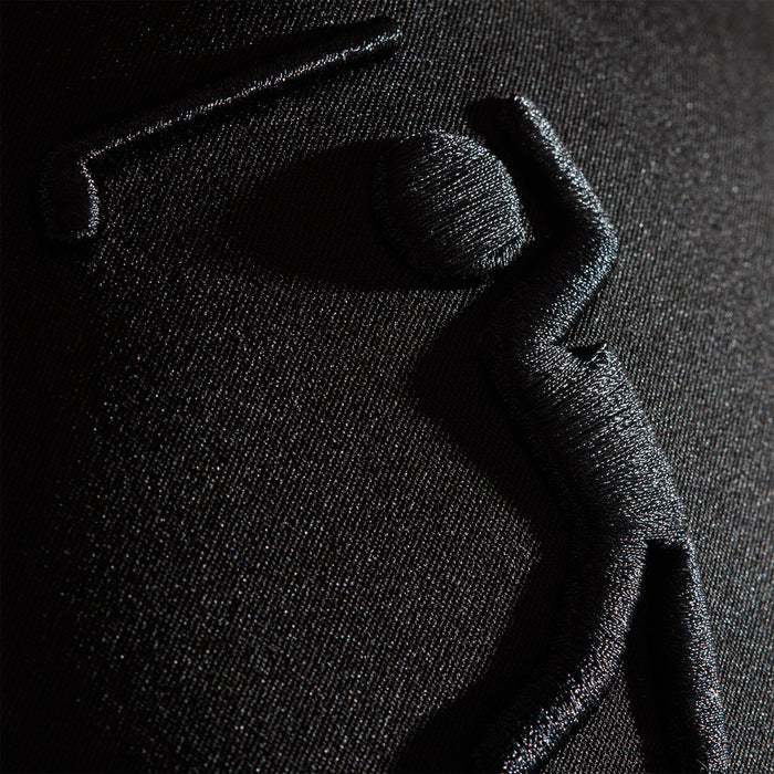 Close-up of the Bogeyman Black/Black Performance Golf Hat's embroidery: a shiny black stick figure, bent at the waist with one arm up and one forward, beneath a stitched horizontal bar on sleek black performance material. Snapback style.