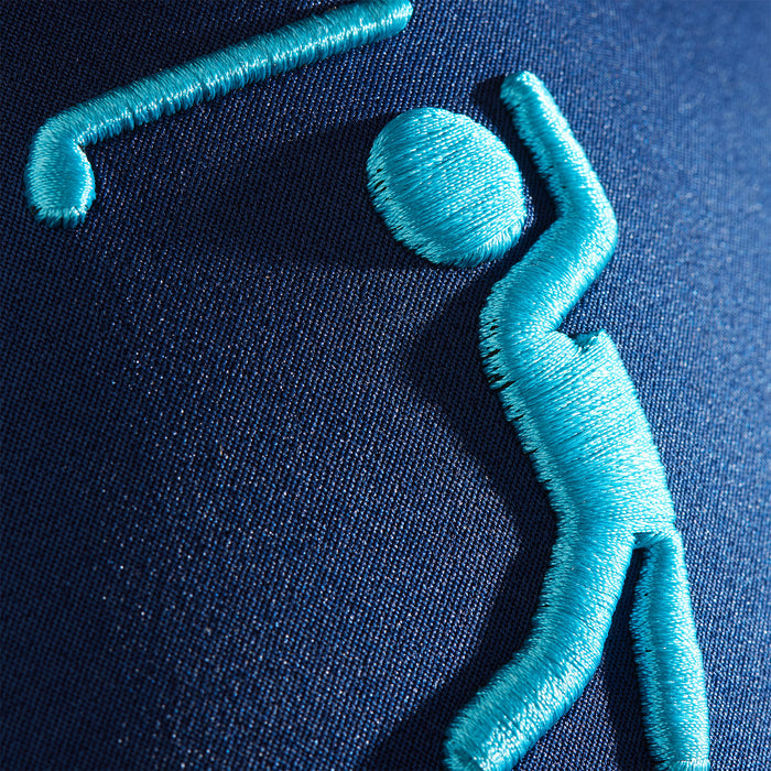 A close-up of light blue embroidery on the Bogeyman Navy/Teal Performance Golf Hat shows a stylized golfer swinging a club, stitched with simple curved and straight lines on dark blue performance material.