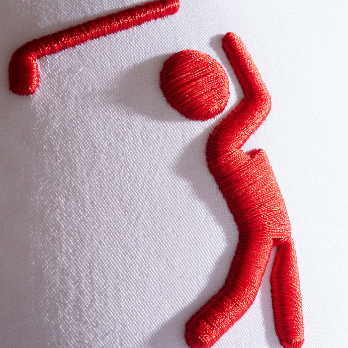 A close-up of the Bogeyman White/Red Performance Golf Hat shows dense, red embroidery on white fabric: a stylized figure with one arm bent and the other raised, holding a boomerang. Smooth stitches give it a bold, textured look.