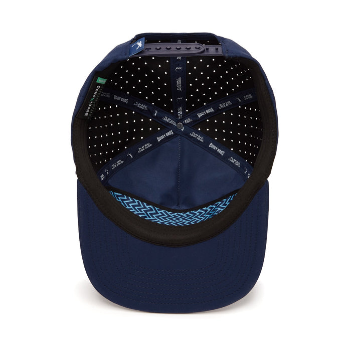 The image shows the inside of the Bogeyman Stamp Navy Unstructured Flat Bill Hat, featuring performance material, a black inner band, white ventilation holes, blue zigzag fabric above the bill, and an adjustable snapback strap.