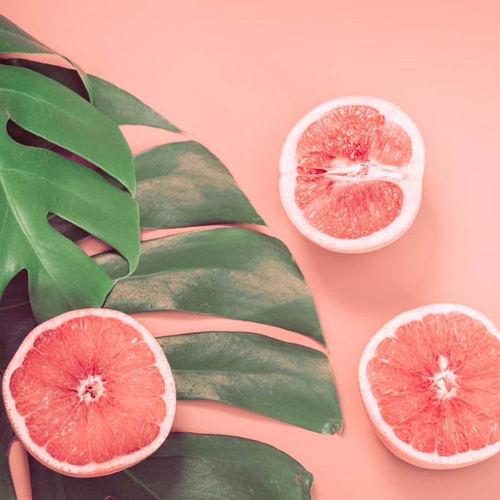 Fresh grapefruit halves arranged on a large green tropical leaf background, evoking natural ingredients and skincare themes for Clarifying Face & Body Oil | Privai.