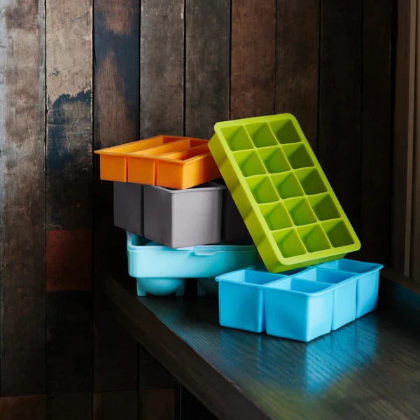 Various ice trays for cocktails on dark moody wooden background.