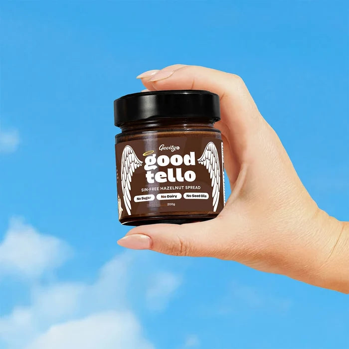 Jar of Gevity goodtello hazelnut spread held in a person's hand against a blue background.