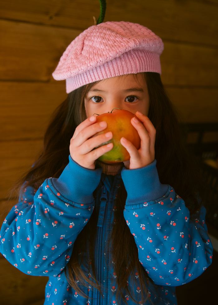 Children in a blue thermal jacket with a floral print and a bright red knitted hat.