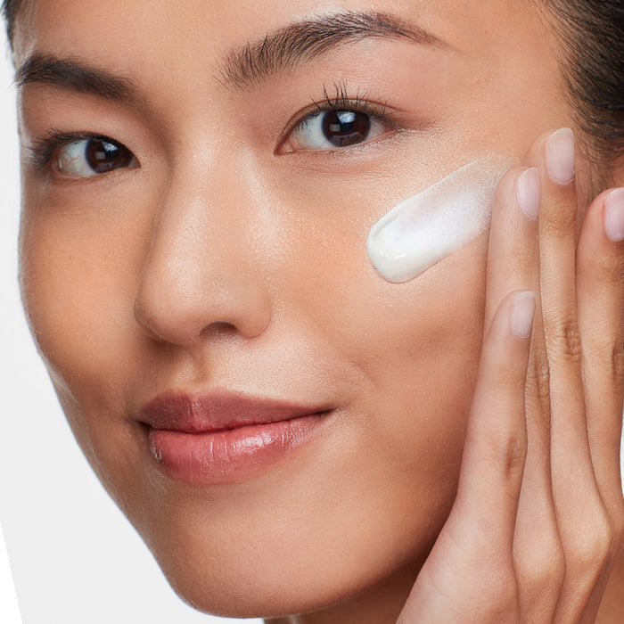 Close-up of a woman gently applying Solar Dew SPF Mineral Serum | HydroPeptide to her smooth skin, highlighting skincare and wellness.