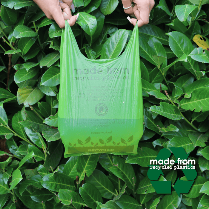 Hands holding a green Ancol 'Made from' poop bag filled with water to show that it's leak proof. In the background is a hedge.