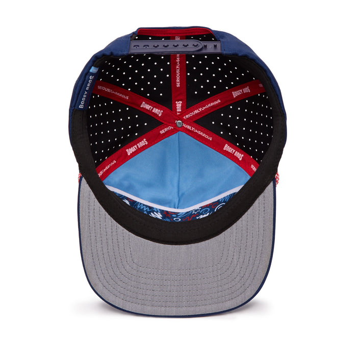 The image shows the inside view of a baseball cap. The cap’s interior lining includes red taped seams with white text, black fabric with white polka dots, and a blue section. The brim is gray on the underside with a patterned blue inner band.