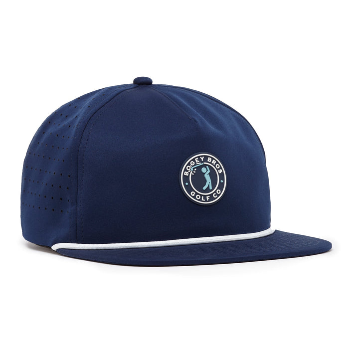 The Bogeyman Stamp Navy Unstructured Flat Bill Hat features a snapback closure, adjustable flat brim, white-trimmed edge, circular Bogey Bro Golf Co. logo patch, side ventilation holes, and classic top button in performance fabric.