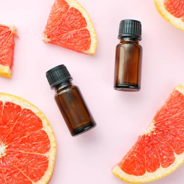 Two small amber glass bottles with black caps surrounded by fresh grapefruit slices, representing the skincare product Clarifying Face & Body Oil | Privai.