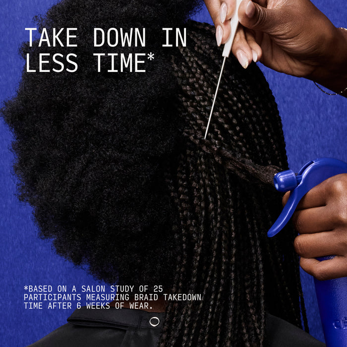 Hand holding spray bottle applicating liquid to braided hair against blue background.