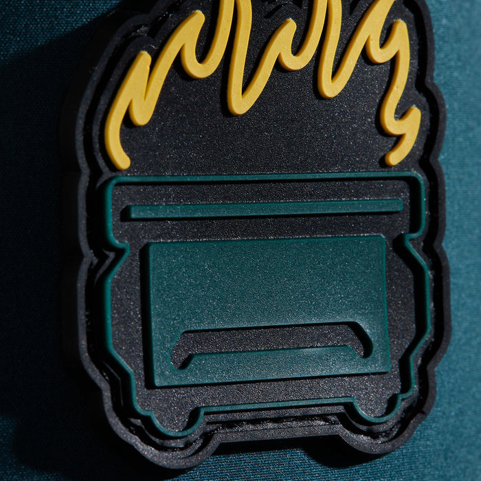 The Dumpster Fire - Unstructured Flat Bill Hat - Snapback features a rubber patch of a green dumpster with yellow flames and bold black outlines on a textured teal base—making it the perfect eye-catching accessory for your hat collection.
