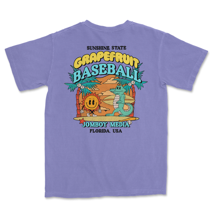 Lavender Comfort Colors T-shirt featuring a colorful Grapefruit Baseball design with a sun, palm trees, and cartoon characters.