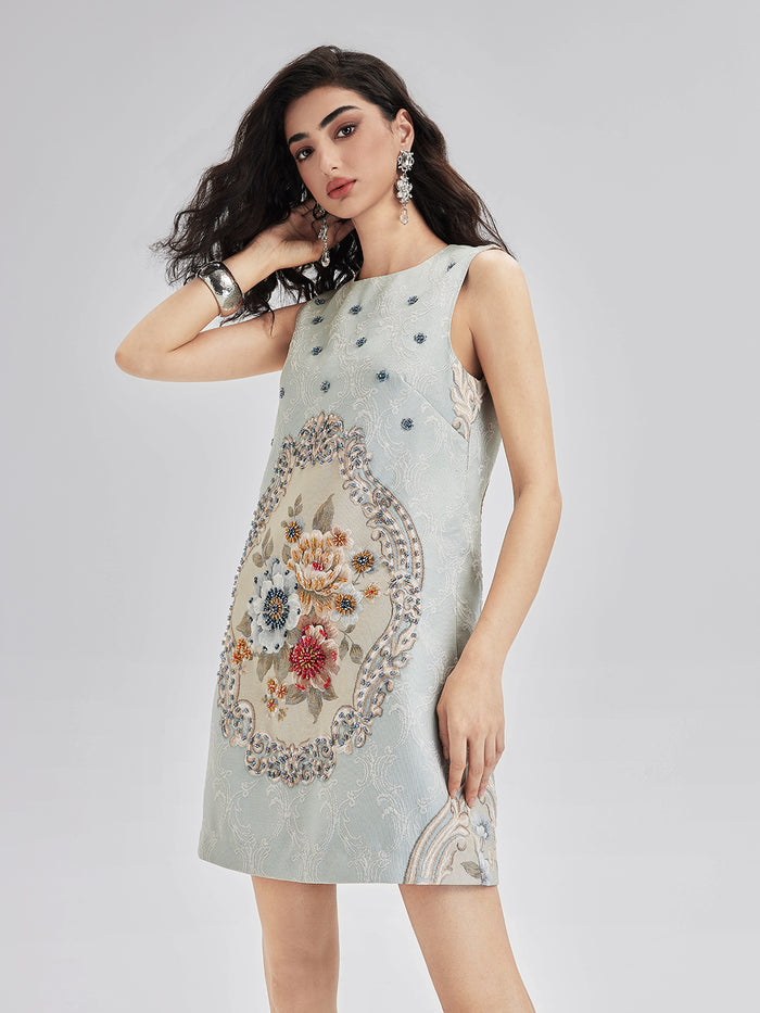 Elegant woman in a light blue sleeveless mini dress featuring intricate floral embroidery and decorative patterns