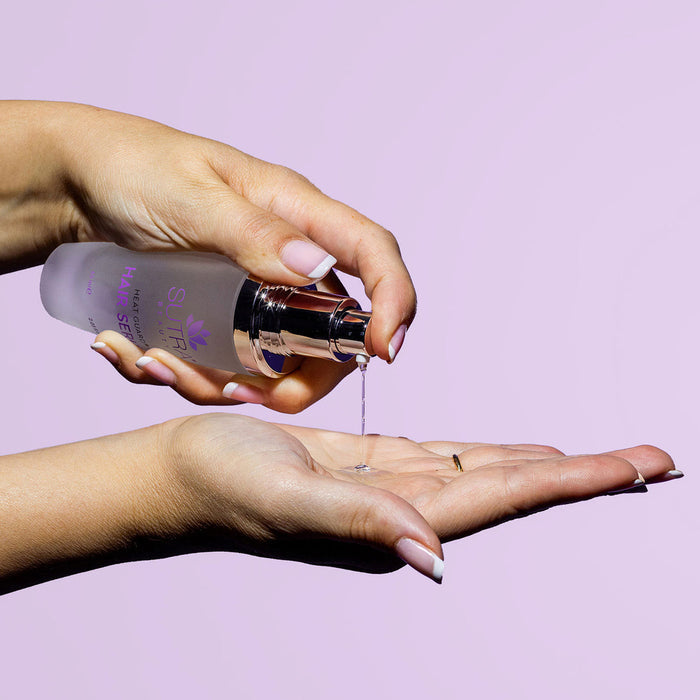 Hands dispensing a clear liquid from a frosted bottle onto an open palm against a purple background, showcasing Heat Guard Hair Serum | SUTRA for hair care and wellness.