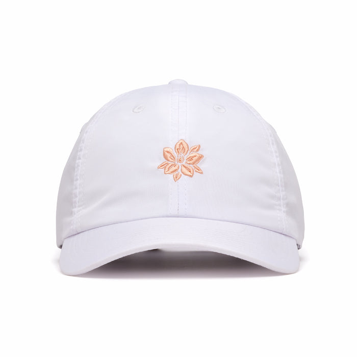 The In Bloom - Dad Hat is a white, six-panel unstructured baseball cap with an adjustable back strap and visible stitching. It features a small, embroidered light peach five-petal flower centered above the brim.