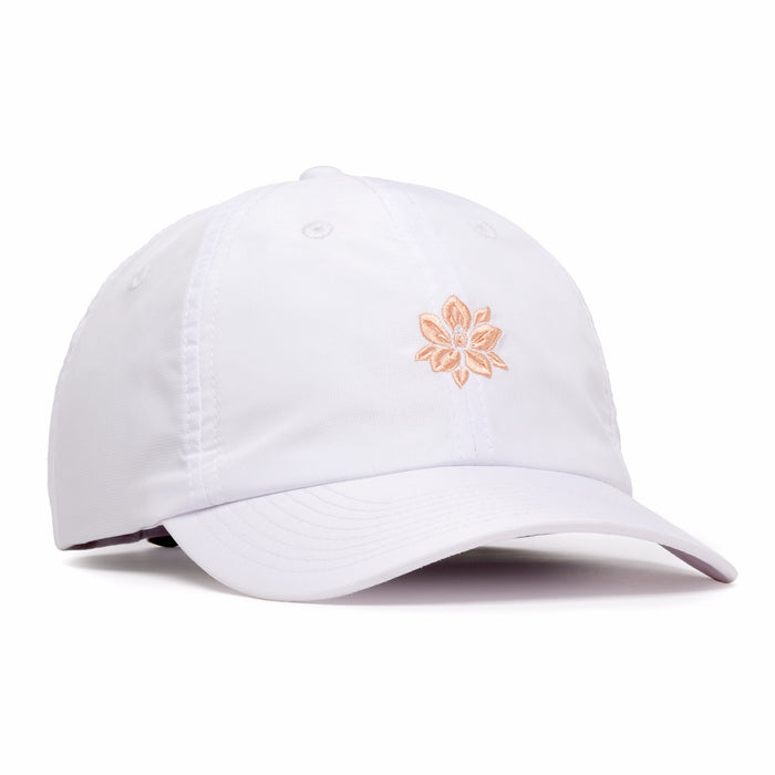 The In Bloom - Dad Hat is a white baseball cap with a curved brim, light pink embroidered flower on the front, ventilation eyelets, adjustable back strap, and a sweatband for comfort.