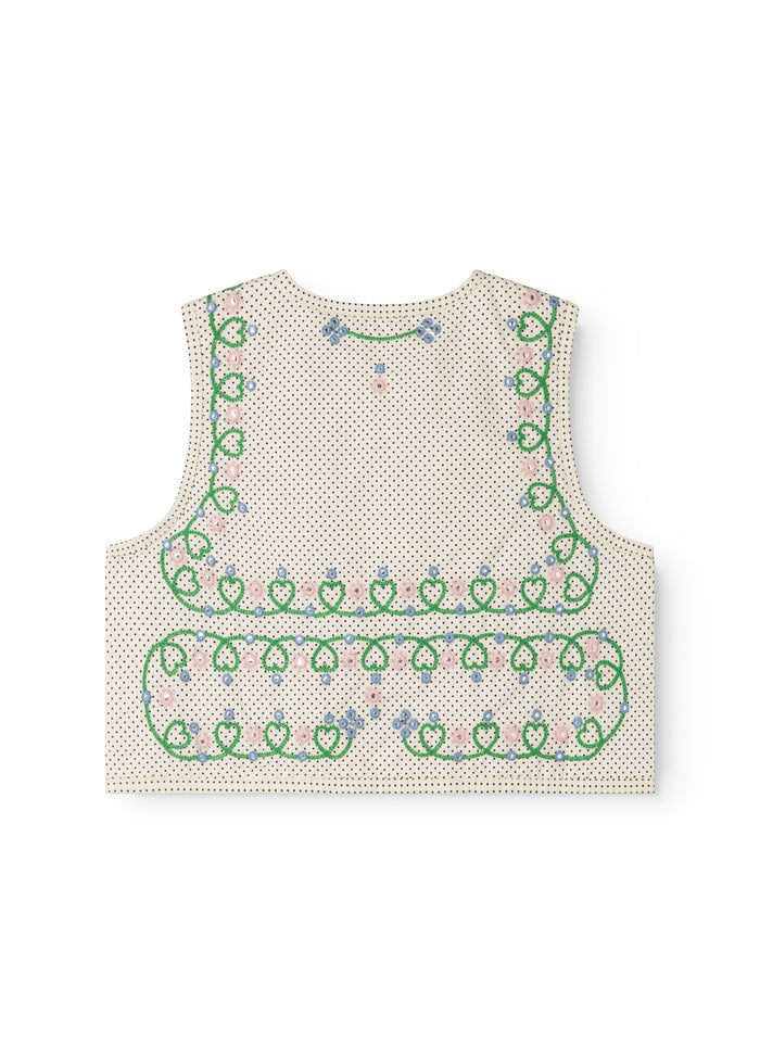 Bag side of a dotted children's vest with green embroidery and blue/pink flowers.