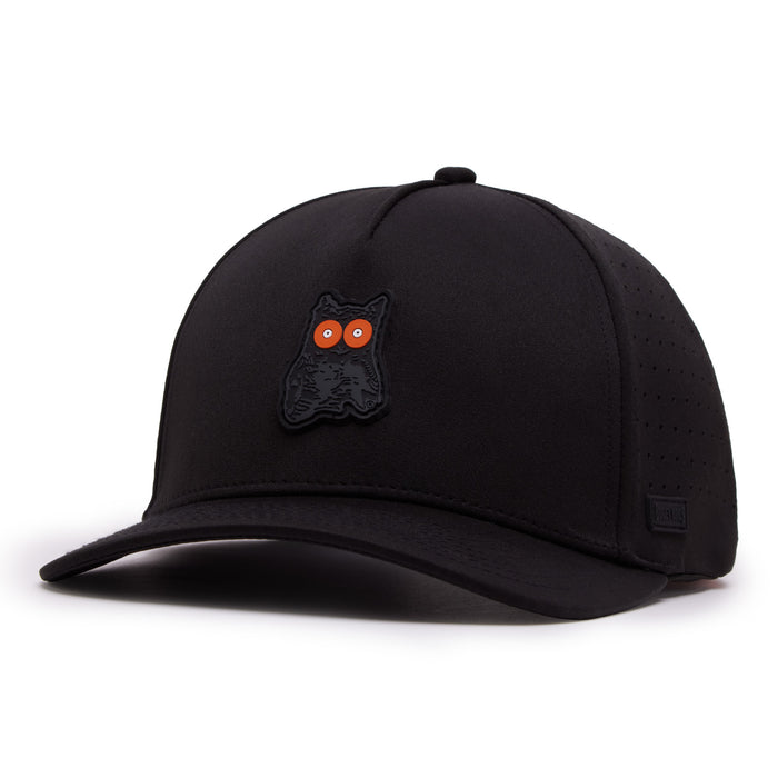The Night Owl Performance Golf Hat is a black snapback with a curved brim, perforated side panels, and a raised black owl patch with vivid orange eyes. Made from performance material, it features a subtle black logo tag by the brim.