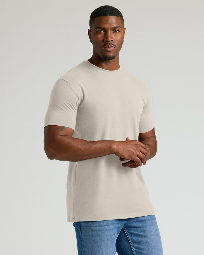 Man wearing a beige t-shirt and blue jeans on a plain background