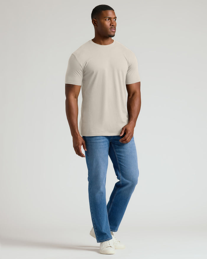 Man wearing a beige t-shirt and blue jeans on a white background
