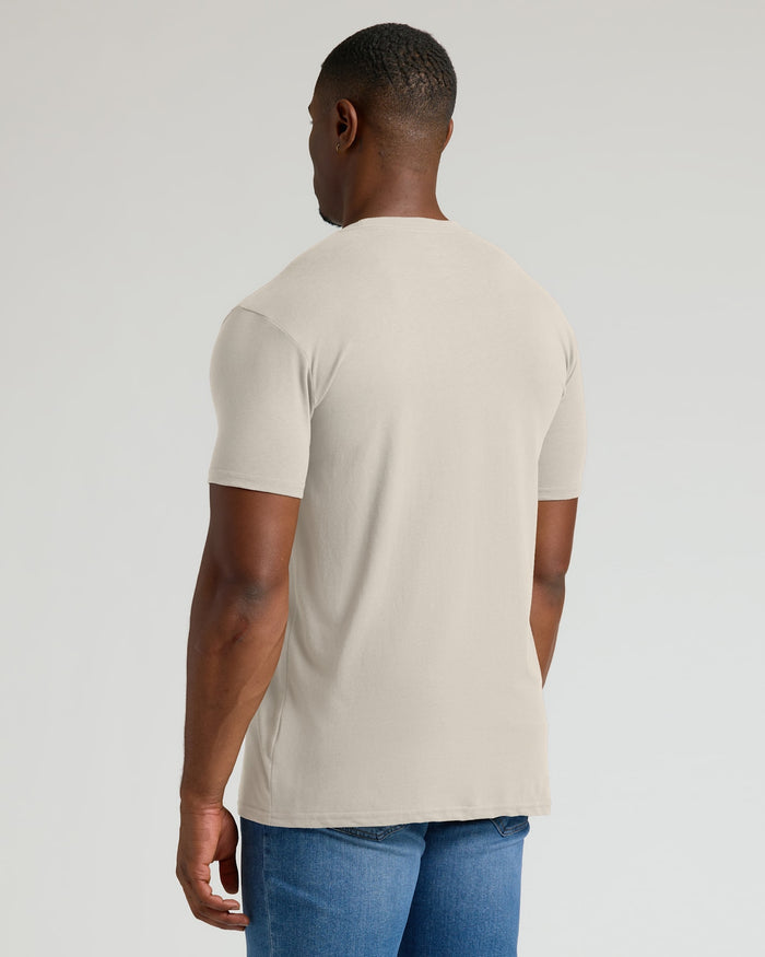 Man wearing a beige t-shirt and blue jeans on a light gray background