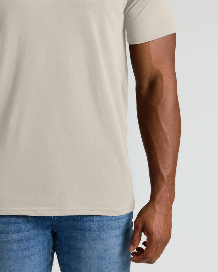 Person wearing a beige t-shirt and blue jeans on a plain background