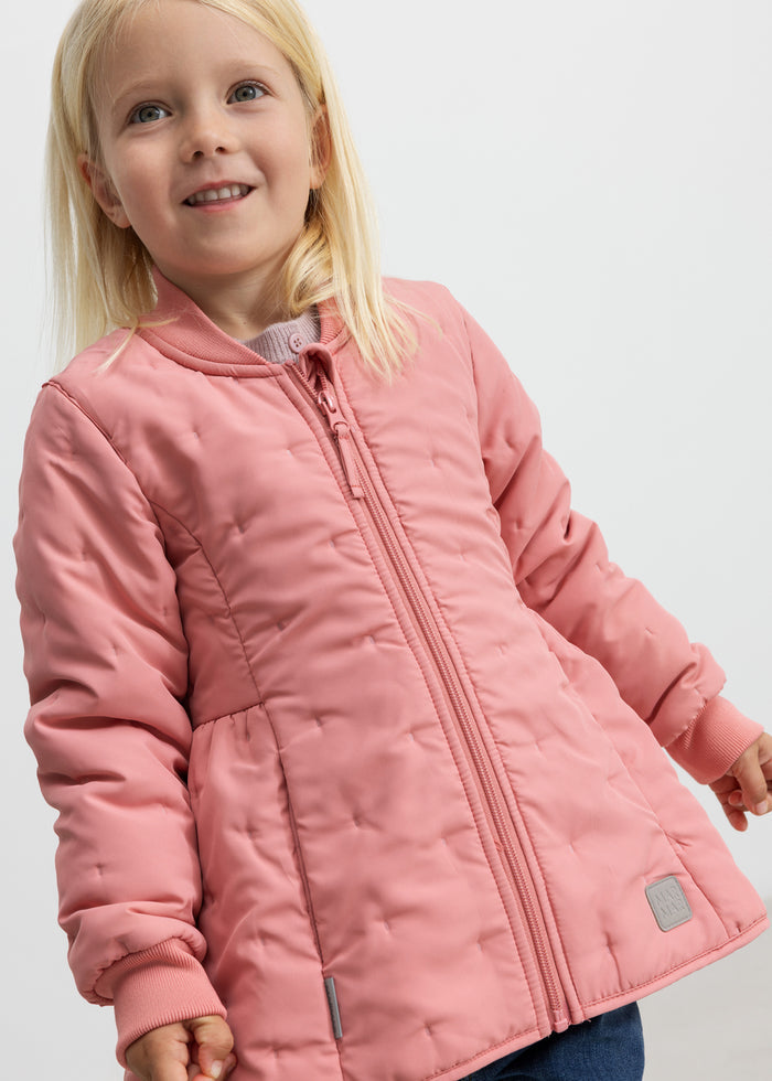 Child wearing pink thermal jacket, smiling and with hand in pocket