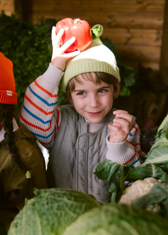 Child wearing a green quilted vest and striped sweater in the kitchen garden.