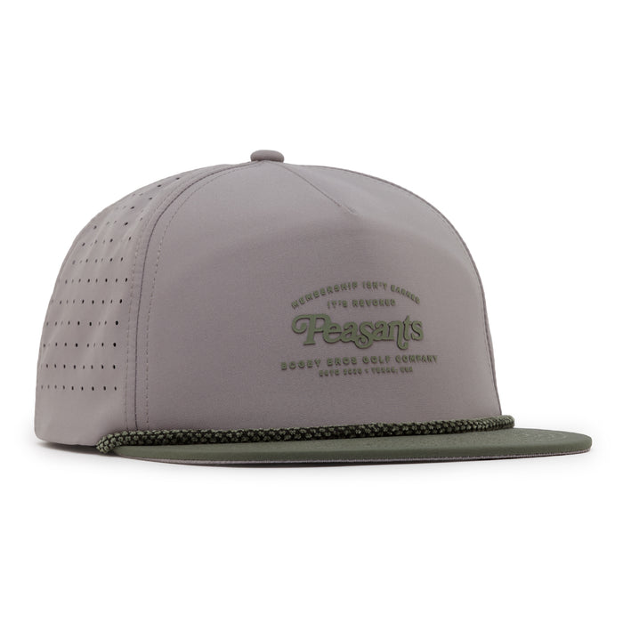 The Revoked Unstructured Flat Bill Hat is a light gray snapback with an olive green flat brim, perforated side panels, green "Peasants" embroidery on the front, smaller text, and a decorative cord across the base of the brim.