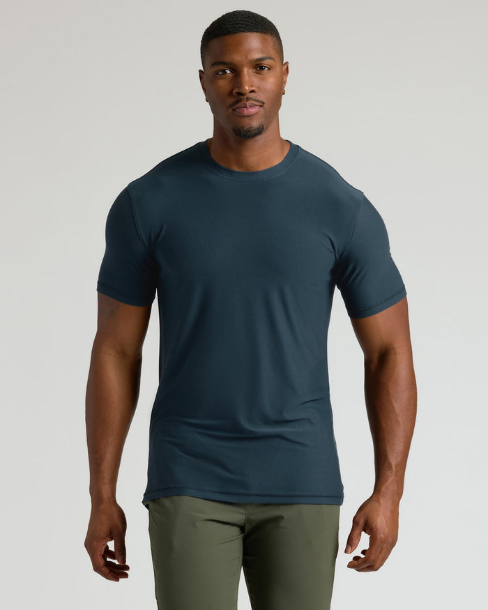 Man wearing a dark blue t-shirt and green pants on a light gray background
