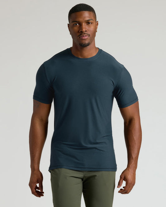 Man wearing a dark blue t-shirt and green pants on a light gray background