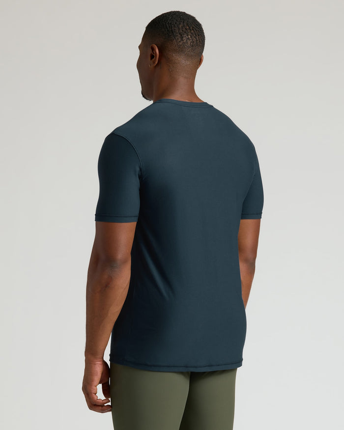Man wearing a dark blue t-shirt and green pants on a light gray background