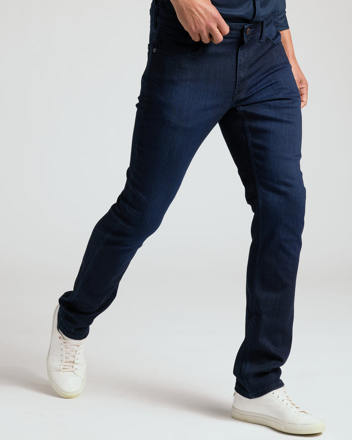 Person wearing indigo jeans and white sneakers on a light gray background