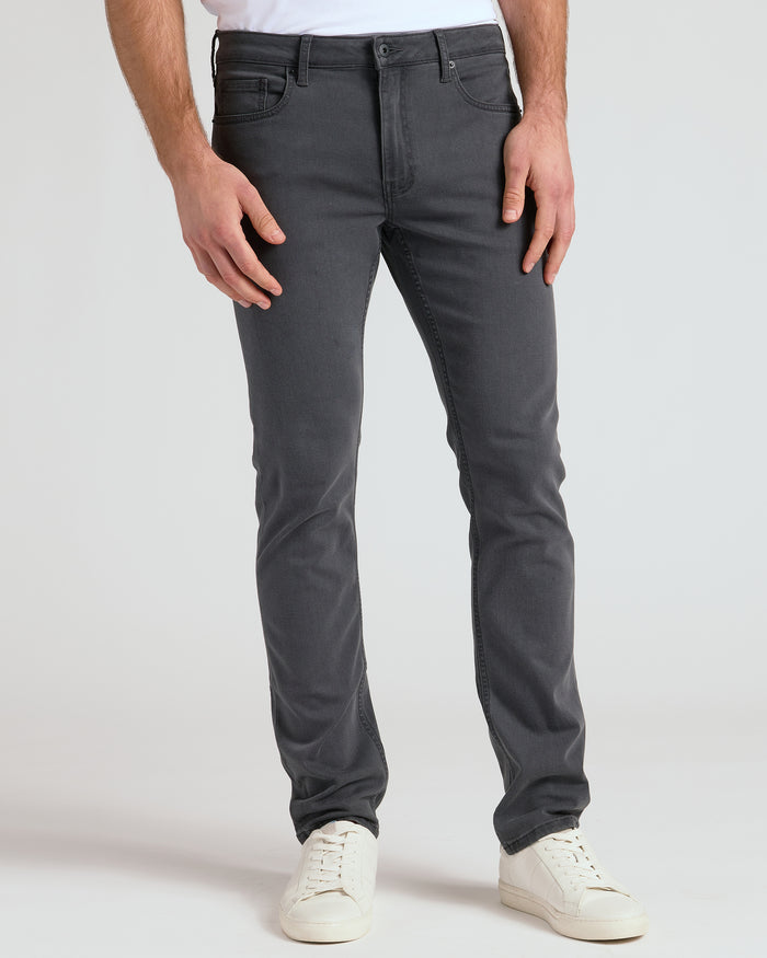 Person wearing dark gray jeans and white sneakers on a light gray background