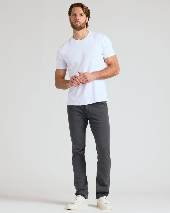 Man wearing a white t-shirt and dark gray pants on a light gray background