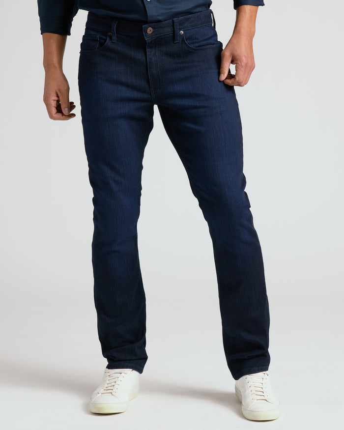 Person wearing dark blue jeans and white sneakers on a plain background