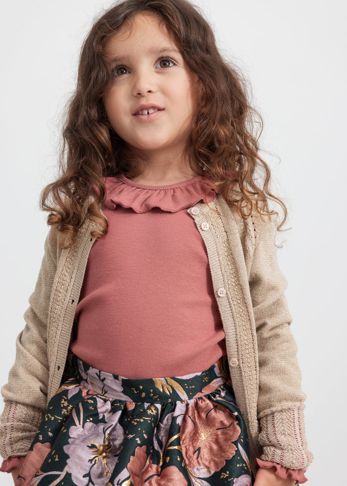 Girl wearing dark green skirt with floral print, pink blouse and beige cardigan for children