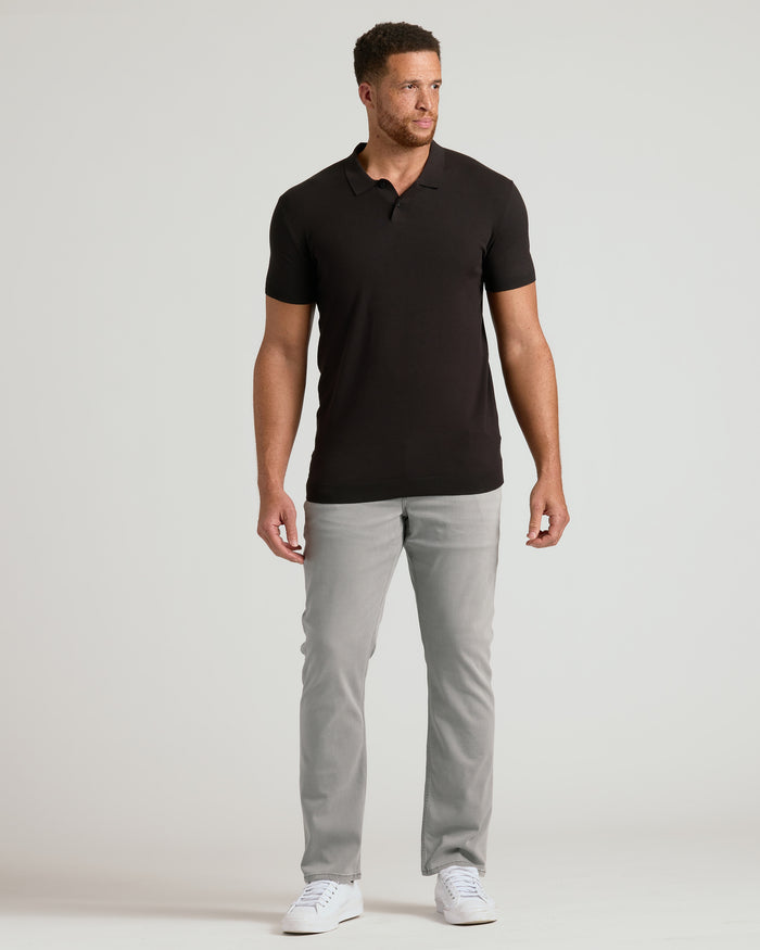 Man wearing a black polo shirt and gray pants on a white background
