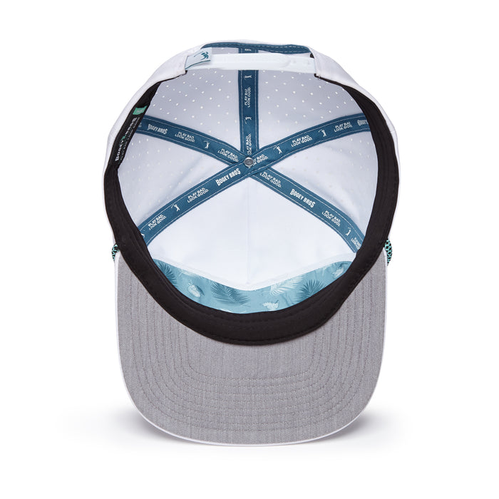 A top-down view of the Tiki Flat Bill Unstructured Flat Bill Hat shows its light gray brim, adjustable snapback, teal inner band with Benny Gold text, white dotted lining, and teal fabric featuring subtle leaf patterns.