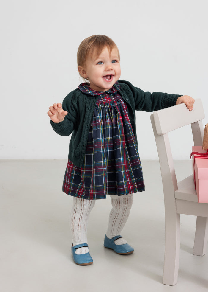 Baby wearing dark green cardigan with lace pattern and checkered red and green Christmas dress