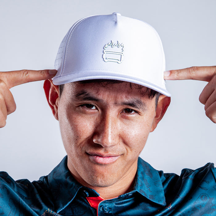 A man in a blue patterned shirt points at his "White Hot - Performance Golf Hat - Snapback," which shows a stylized burger with flames. Made from sweat stain resistant material, he looks confidently into the camera.